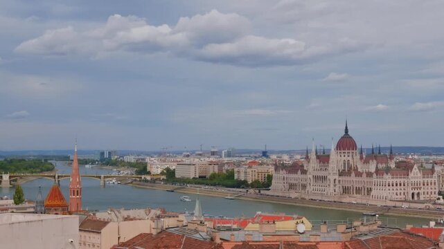 Flat light lies over the rooftops and the river, the Parliament pale on the far bank and a bridge upstream in the haze. Elevated view from Castle Hill, pan right.