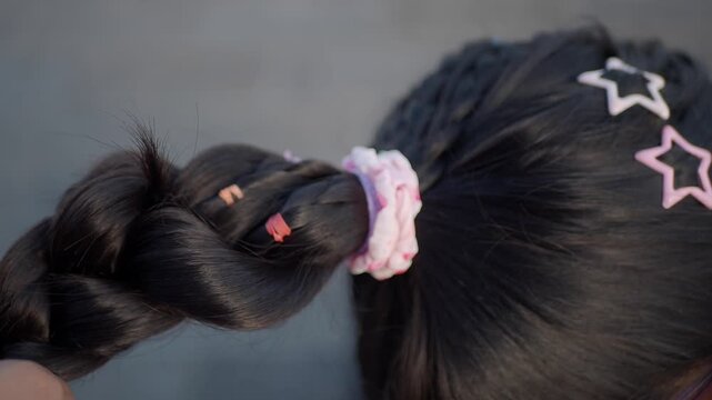 Person braiding long black hair with clips and a pink scrunchie
