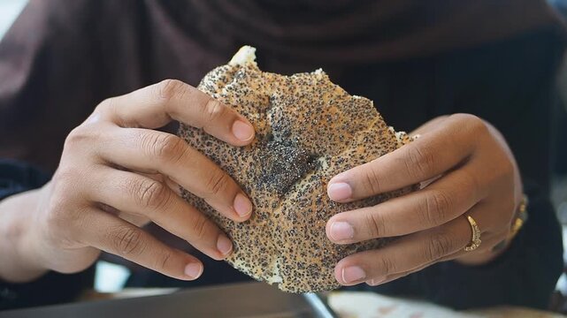 Person holds a piece of seeded flatbread with both hands indoors