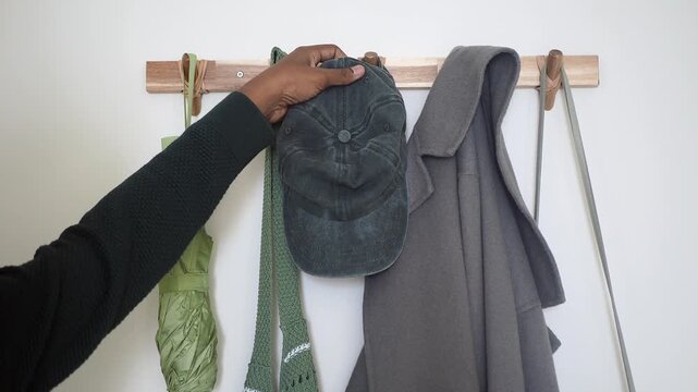 Cap, coat, and umbrellas hanging from a wooden wall rack indoors