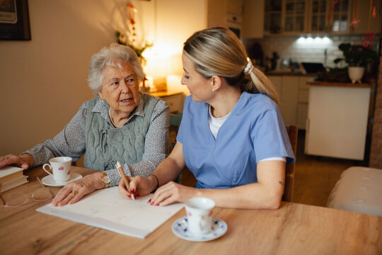 Social worker helping elderly lady with managing her finances, working on financial plan.