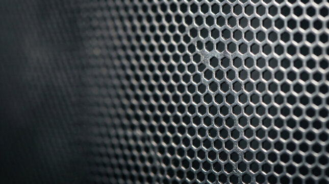 Close up macro view of brushed silver industrial ventilation mesh screen featuring a repeating honeycomb pattern with metallic texture, shallow depth of field, and dramatic ambient studio lighting.