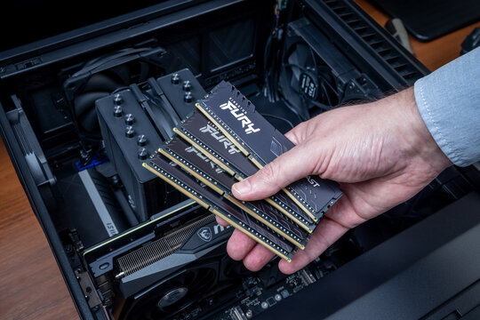 Technician holding four Kingston Fury DDR modules in front of an open PC case with high-end components. PC assembly or upgrade. Pavlodar, Kazakhstan - December 15, 2025