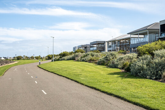 A wide shared pedestrian and cycling path at Werribee South, Victoria, Australia, beside a manicured green lawn and native coastal shrubs and modern new houses. Upmarket coastal development
