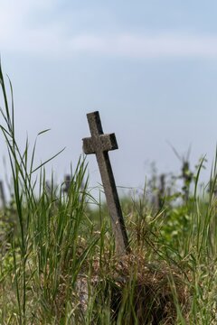 Gravestone cross in overgrown grass