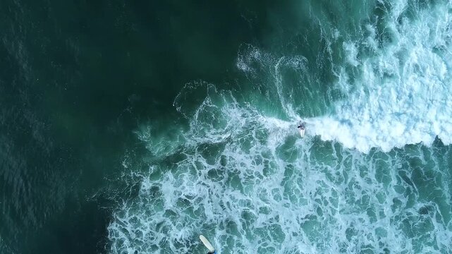 Inspiring top-down drone view of surfers paddling in clear turquoise sea surrounded by ocean wave foam. Excellent intro scene for sports documentaries and travel videos.