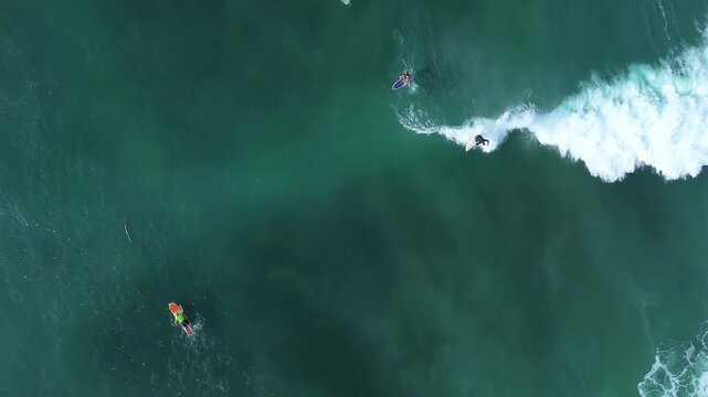 Overhead aerial landscape of tropical ocean lineup with surfers paddling and riding white foaming waves. Concept of outdoor adventure, ocean freedom, and active travel.
