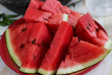 Fresh red watermelon slices with natural black seeds arranged neatly on a red plate © Hendri