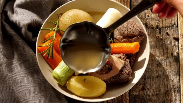 Traditional french pot au feu beef stew with vegetables and broth served with ladle on wooden table