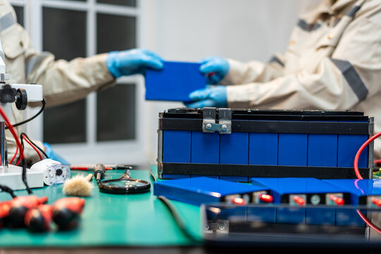 Technicians wearing blue gloves assemble and inspect a blue battery
