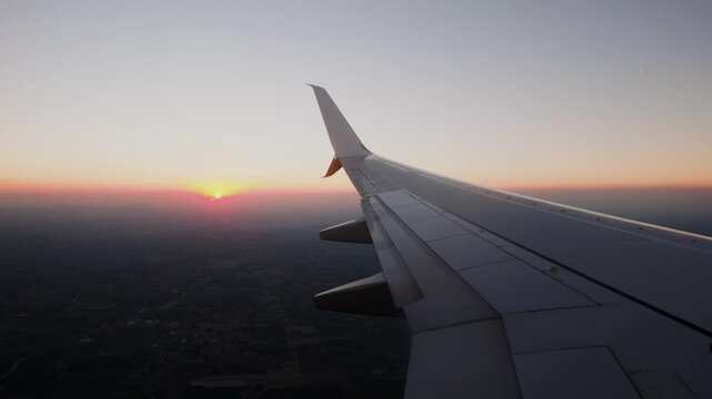 The last of the sun goes down into a band of haze over the plain, the wing dark against the glow. Window seat view, near static.