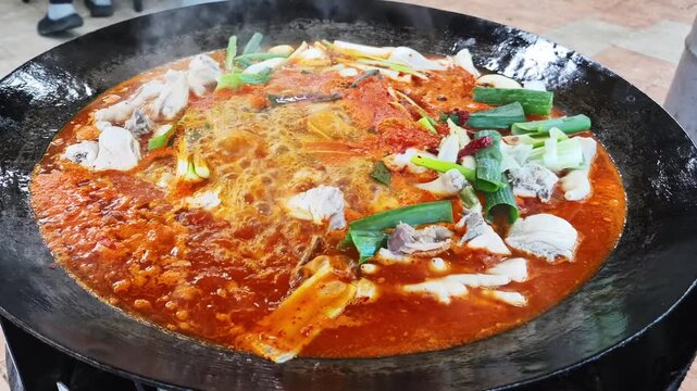 가마솥 뚜껑에서 매콤한 한국식 닭볶음탕이 보글보글 끓고 있는 클로즈업.(Close up of spicy korean braised chicken stew boiling in a large cauldron.)