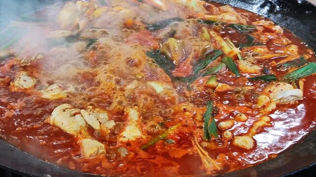 가마솥 뚜껑에서 매콤한 한국식 닭볶음탕이 보글보글 끓고 있는 클로즈업.(Close up of spicy korean braised chicken stew boiling in a large cauldron.)