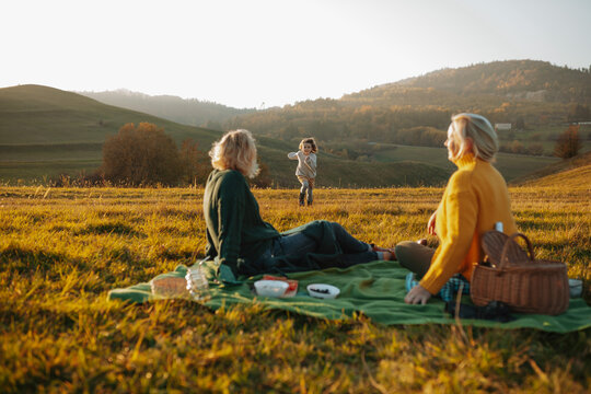 Three generations of women having a picnic on a green autumn meadow at sunset.