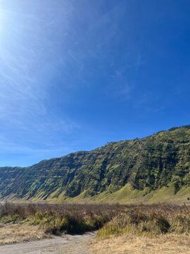 Beautiful landscape of green volcanic cliffs and savanna valley under a clear blue sky in Mount Bromo Tengger Semeru National Park, East Java, Indonesia.
