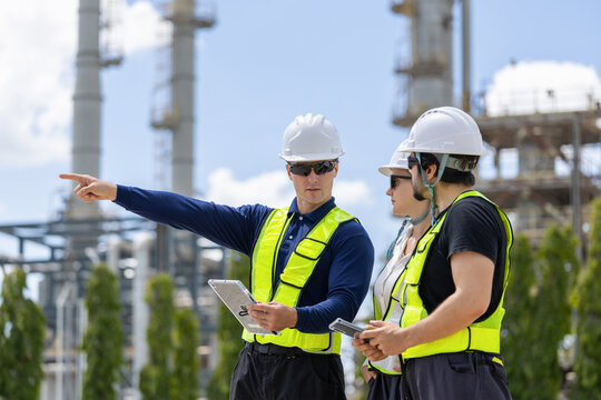 Group of industrial engineers holding digital tablets during site inspection at chemical refinery, Engineering team in safety vests and hard hats discussing refinery plant operation outdoors