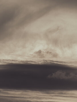 Dramatic layered clouds in warm sepia tones with soft light breaking through, moody atmospheric skyscape background