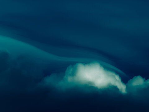 Deep teal and navy blue dusk sky with sweeping wave-like cloud streaks and a single glowing cloud, moody surreal atmospheric background with copy space