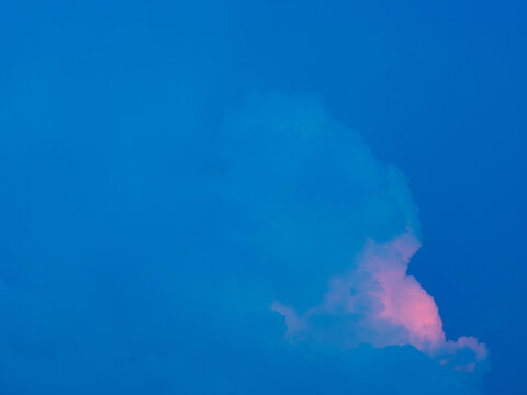 deep blue sky with a single cloud glowing pink at its base at dusk, minimalist dreamy sunset background with generous copy space