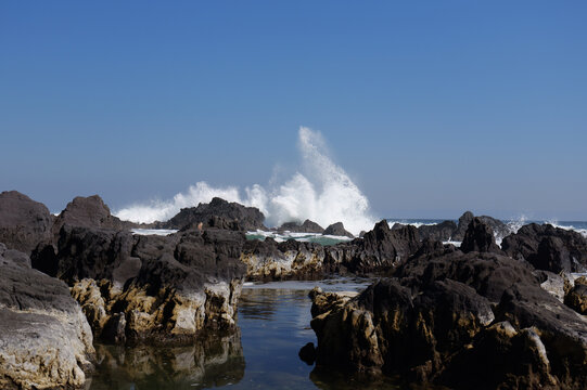 Big wave splashing over volcanic rocks and tide pool in Manazuru