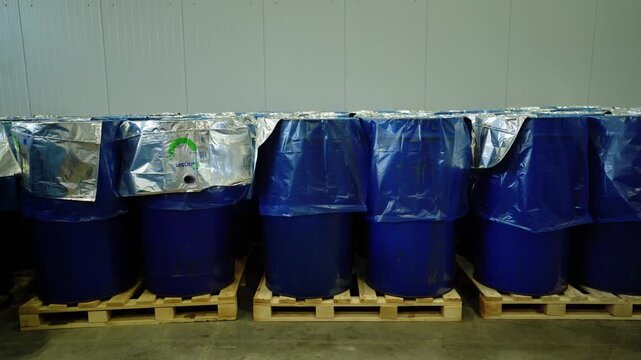 Stacked blue drums wrapped in silver liners on wooden pallets