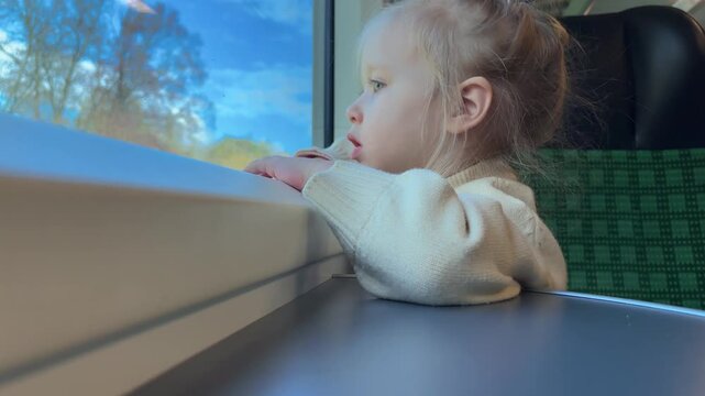 A girl rests her arms on a train table and watches the passing landscape, childhood travel, quiet journey, everyday discovery.