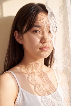 Portrait of woman with lace shadow pattern from curtain on face for romantic editorial banner and soft background design