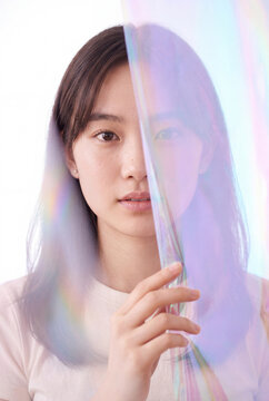 Portrait of young woman behind iridescent film with pastel light reflections for creative background and beauty banner design