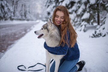 Red-haired girl crouching and hugging a husky dog on snow © Nomad_Soul