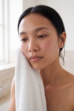 Woman drying her face with a towel after cleansing with water droplets for gentle skincare routine and face care background