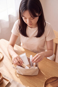 Woman organizing travel size skincare products into pouch for minimalist beauty routine background and cosmetic packing guide