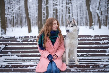 Smiling red-haired girl sitting next to a husky dog on a bench © Nomad_Soul