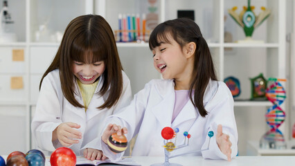 Two Happy Schoolgirls in Lab Coats Studying Solar System Model © blueringmedia