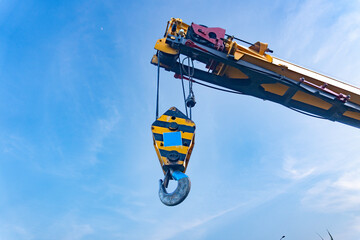 Crane hook hanging from boom against blue sky background © Muhamad