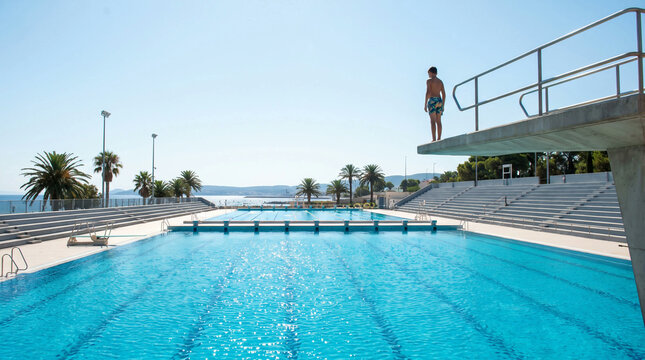 Young Boy Standing on Diving Board Overlooking Large Outdoor Swimming Pool