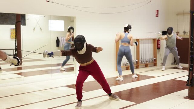 Male and female fencers wear fencing masks practicing sparring fights together in pairs in sports hall 