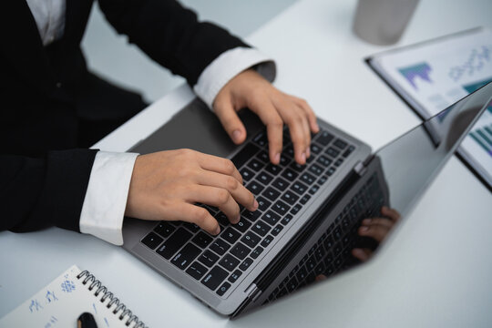 Businessperson typing on laptop keyboard in office workspace with documents and notebook on desk