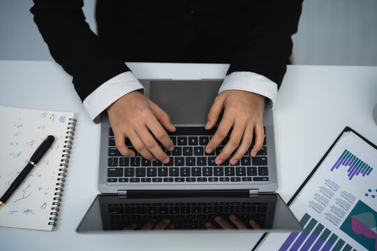 Top view of professional business person typing on laptop keyboard with documents and notebook on white desk