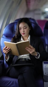 Businesswoman writing and reading in notebook while traveling by airplane.