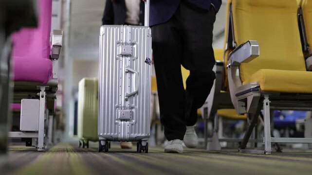 Business couple walking down the airplane aisle with luggage. Asian business man and woman in suits walking down the airplane aisle. The couple is pulling trolley bags, ready for their business trip.