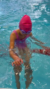 Happy little girl in pink swim cap and goggles playing in an indoor swimming pool. Childhood activities, swimming lessons, sports, and healthy lifestyle