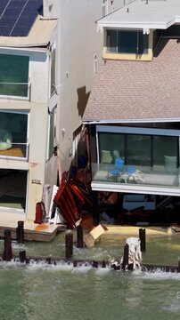 Long Beach, California, USA - October 15, 2026: Slow vertical pan left from a gutted lower floor to a cracked, separating wall and shattered windows of a beach house after Tropical Storm Rachel.