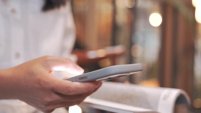 Woman using smartphone to send emails, text messages and research online while reading documents at cozy cafe or study space, business communication, remote work and after work lifestyle concept.