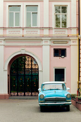 vintage car in court yard vertical picture ornate arched gate pastel facade © Artem Kniaz