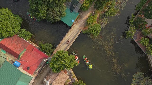 Aerial top down view of tourists riding traditional sampan boats on the ngo dong river. A small bridge crosses the waterway in tam coc