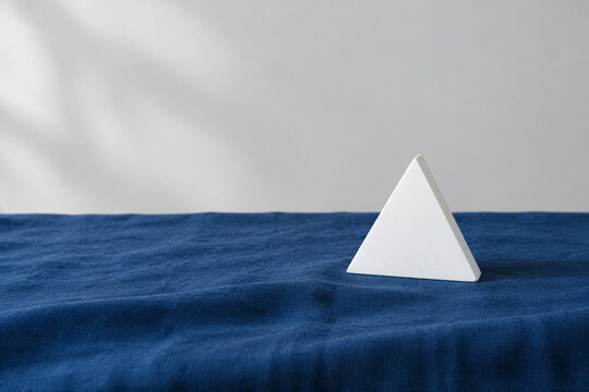 Single white equilateral triangle object on deep blue linen, calm still life for editorial concept