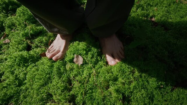 Caucasian adult standing barefoot on soft green forest moss practicing grounding, slow motion top view. Footage suitable for mental wellbeing and mindfulness wellness campaigns