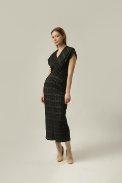 Fashion model wearing a black textured midi dress with a subtle sheen, V neckline and short sleeves, elegant and sophisticated contemporary fall style