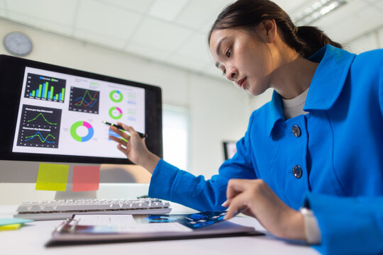 Young businesswoman working on business report, checking charts and graphs on documents and computer screen.