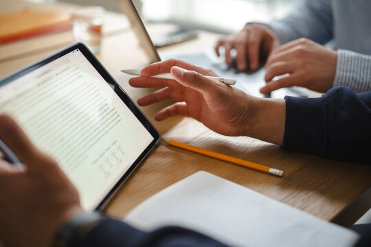 Colleagues collaborate in a modern office, reviewing documents on a digital tablet while another person types on a laptop. They work together on a business project.